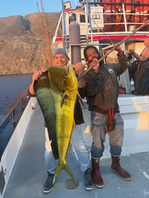 Two crew on the Eldorado deck holding up a bull dorado at sunset