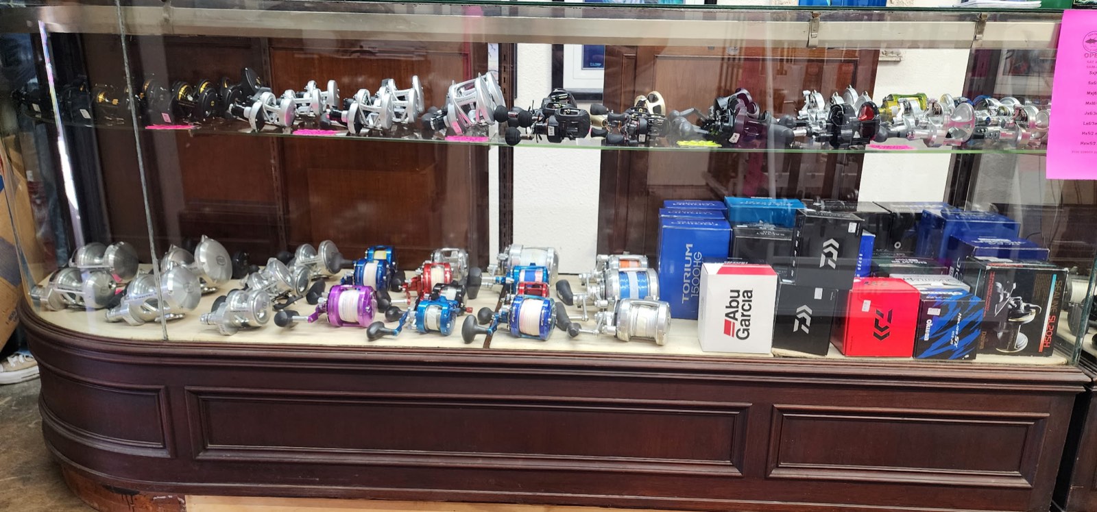 Display case of jigging and casting reels with boxed gear on the shelves behind